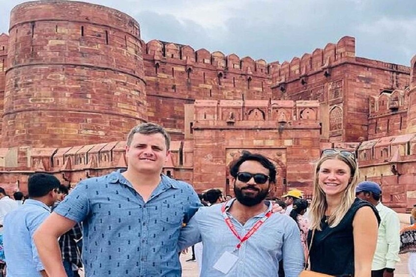 A group of people standing in front of a large, historic red brick fort with intricate architecture. 5