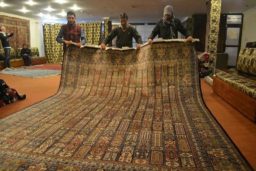 A group of people holding a large, intricately patterned carpet in a room with patterned walls and furniture. 3