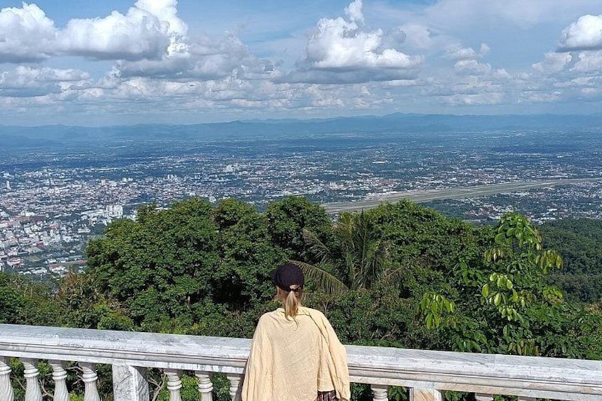 A person standing on a balcony overlooking a cityscape with dense greenery in the foreground. 5