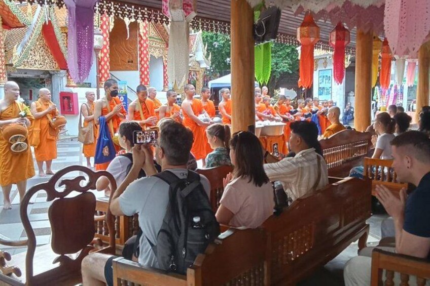 Monjes con túnicas anaranjadas realizando una ceremonia, con espectadores sentados en bancas. 5