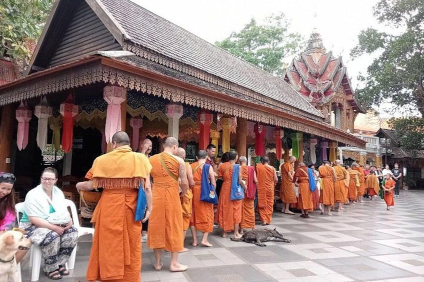 Monks in orange robes standing in a line outside a temple with a traditional roof. 2