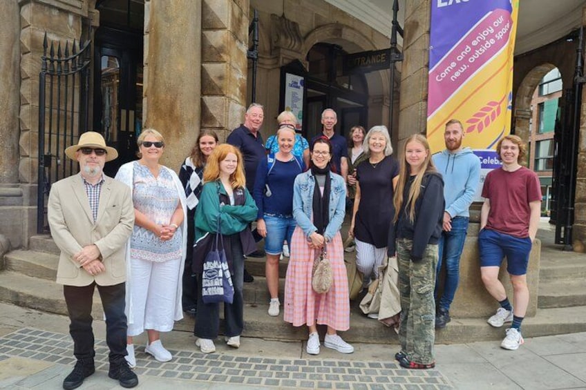 A group of people standing in front of a building with stone columns and a banner. 1