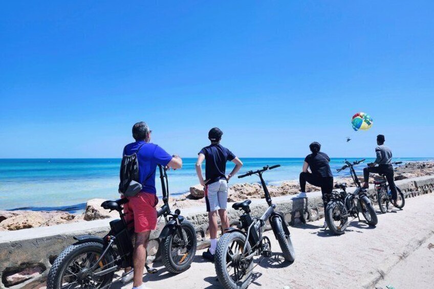 People on bicycles by the beach, a clear blue sky, and the ocean. 5