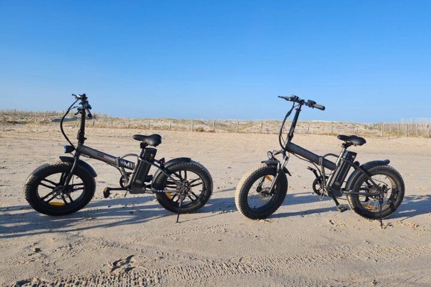 Two electric bicycles parked on a sandy beach with a clear sky. 3
