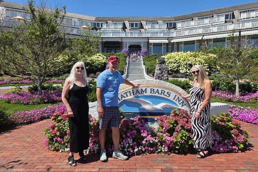 Three people standing in front of a sign for a hotel with a landscaped garden and a building in the background. 2