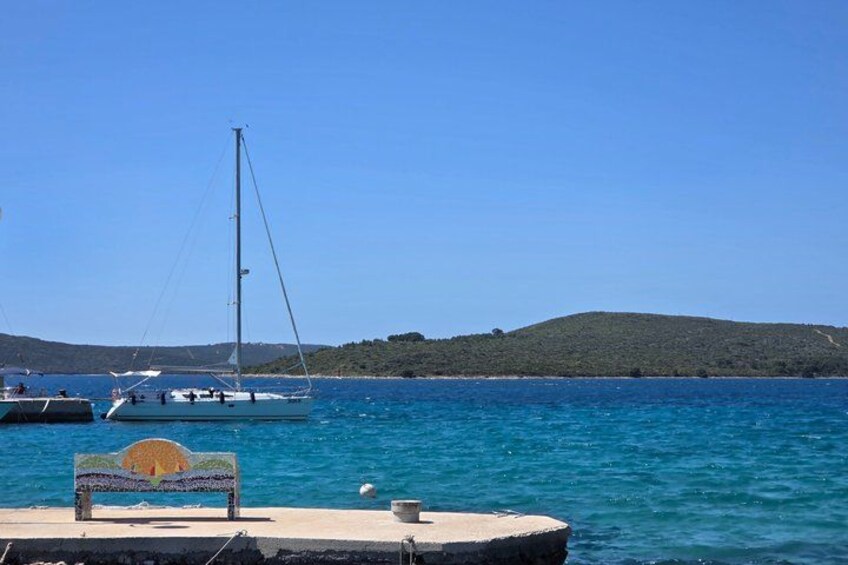 A calm sea with a sailboat, a wooden bench, and a rocky shoreline. 2