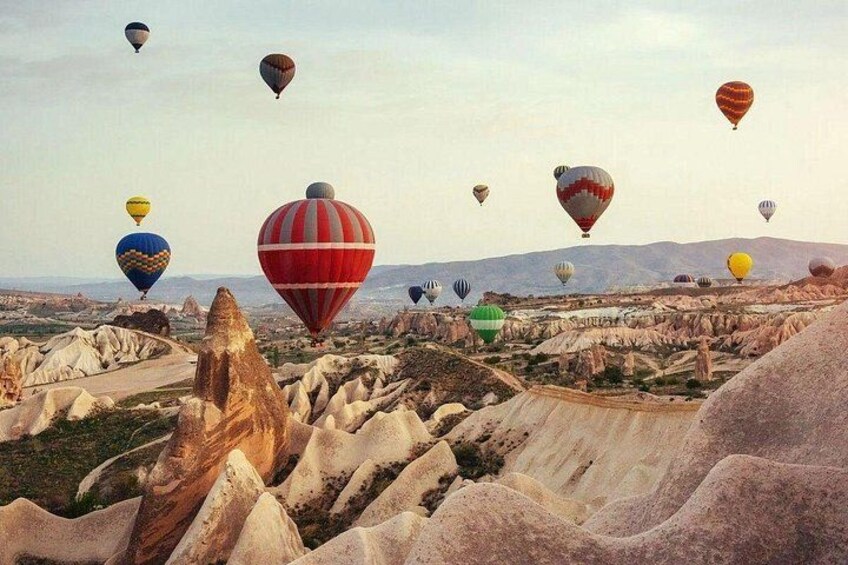 A landscape with numerous hot air balloons in the sky, a winding road, and unique rock formations. 5