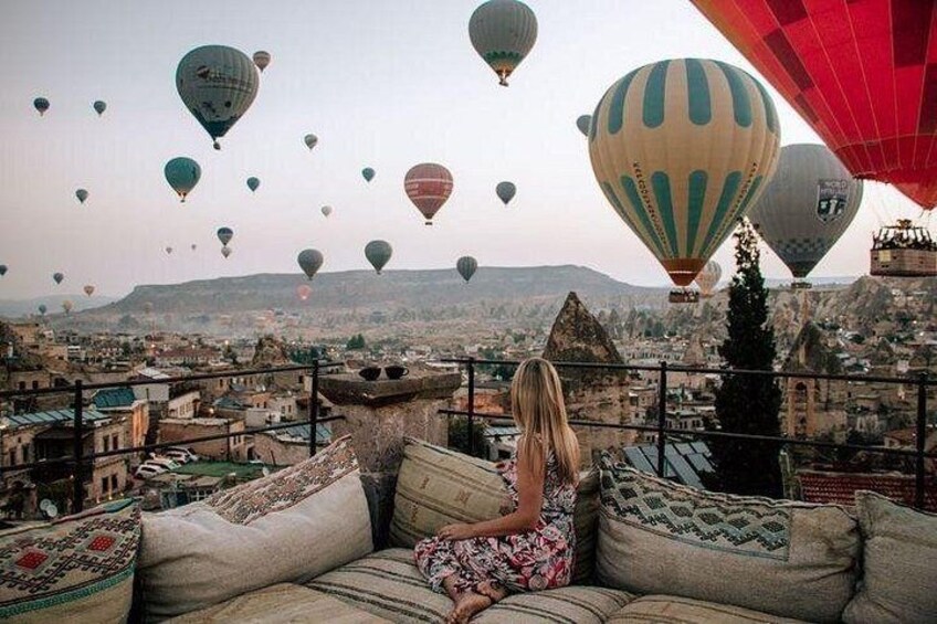 A person sitting on a couch overlooking a cityscape with hot air balloons in the sky. 2