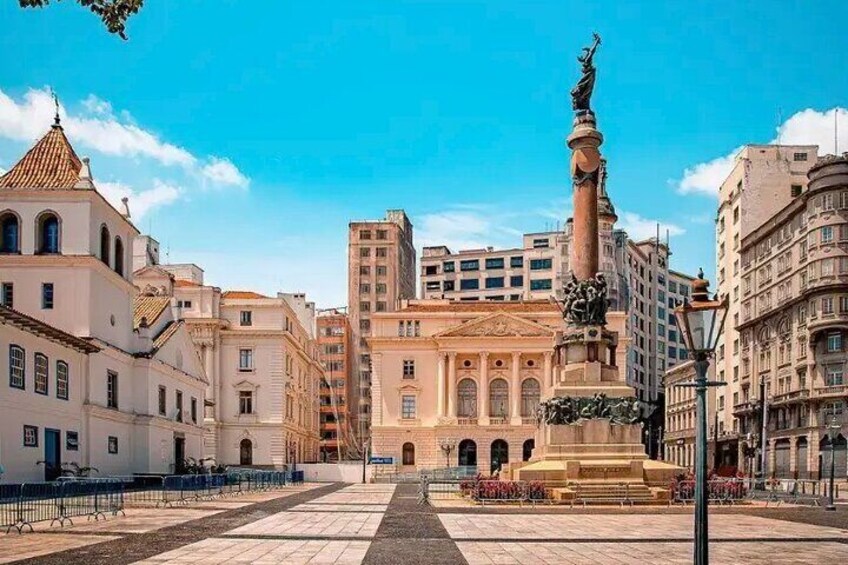 A plaza with a central monument, surrounded by historic buildings and a clear blue sky. 5