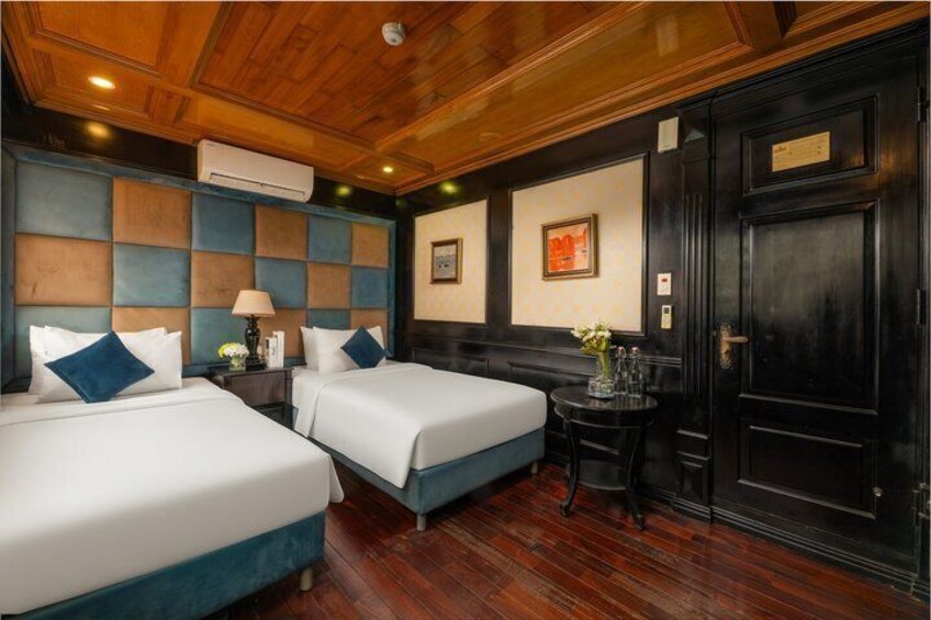 A hotel room with two beds, wooden flooring, a small table with a vase, and a black door. 5