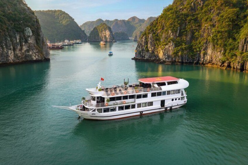 A white river cruise boat with a red roof and multiple decks, navigating through a calm river surrounded by steep, green cliffs. 1