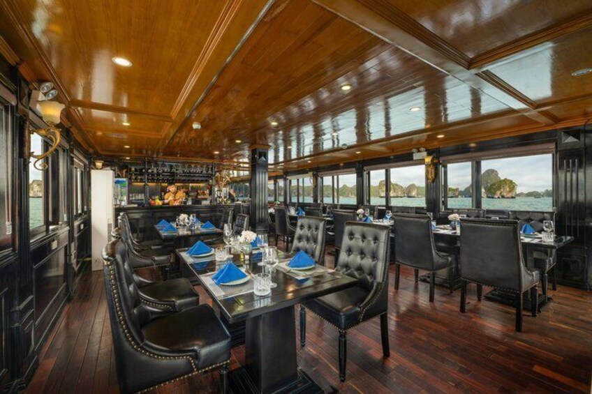 A ship's dining area with wooden interiors, tables set with blue napkins, and a view of the sea through large windows. 2