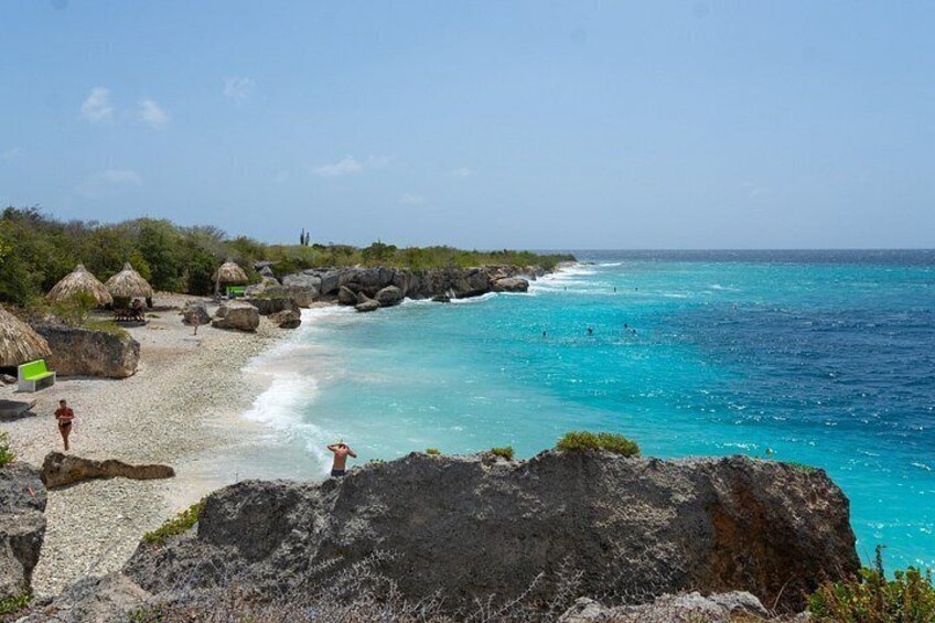A beach with clear turquoise water, rocky outcrops, and thatched-roof huts. 2