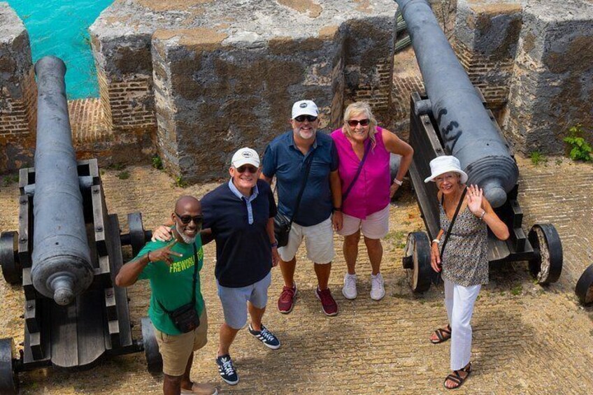 A group of people standing in front of cannons with a body of water in the background. 4
