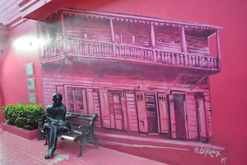 A mural of a pink building with a balcony, a bench, and a statue of a person. 3