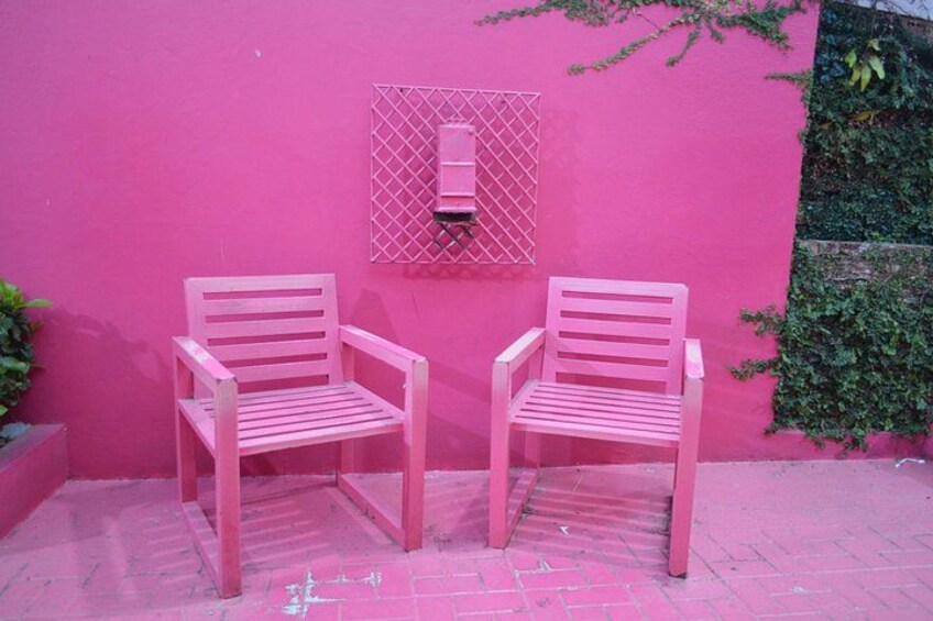 Two pink chairs against a pink wall with a window and greenery. 4
