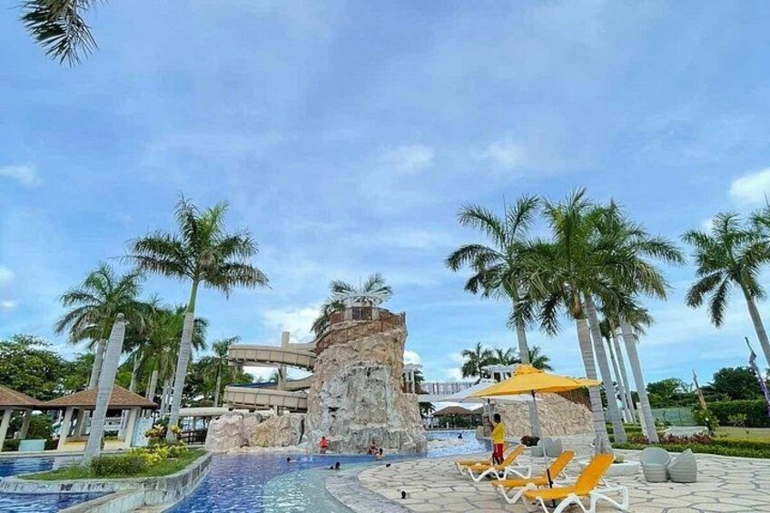 A water park with a large rock formation, palm trees, and lounge chairs. 2