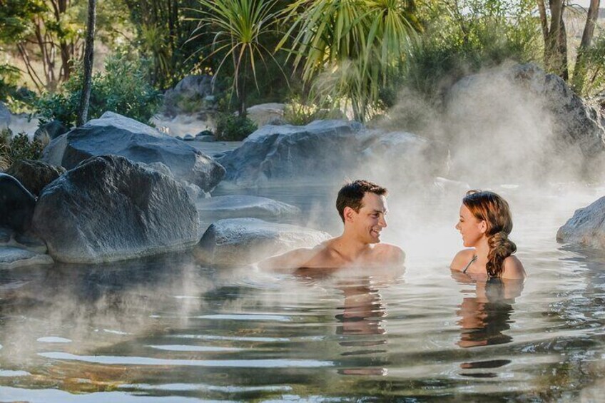A couple in a hot spring surrounded by rocks and greenery. 4