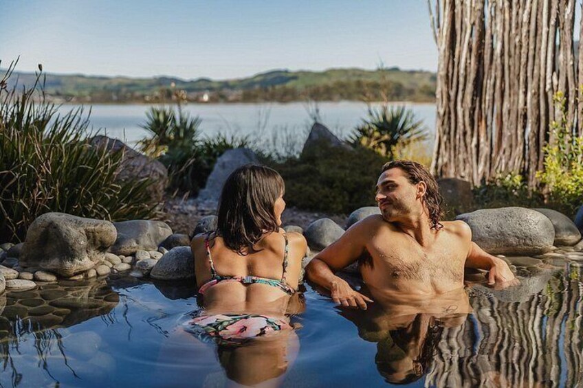 Two people in a natural hot spring surrounded by rocks and plants. 3