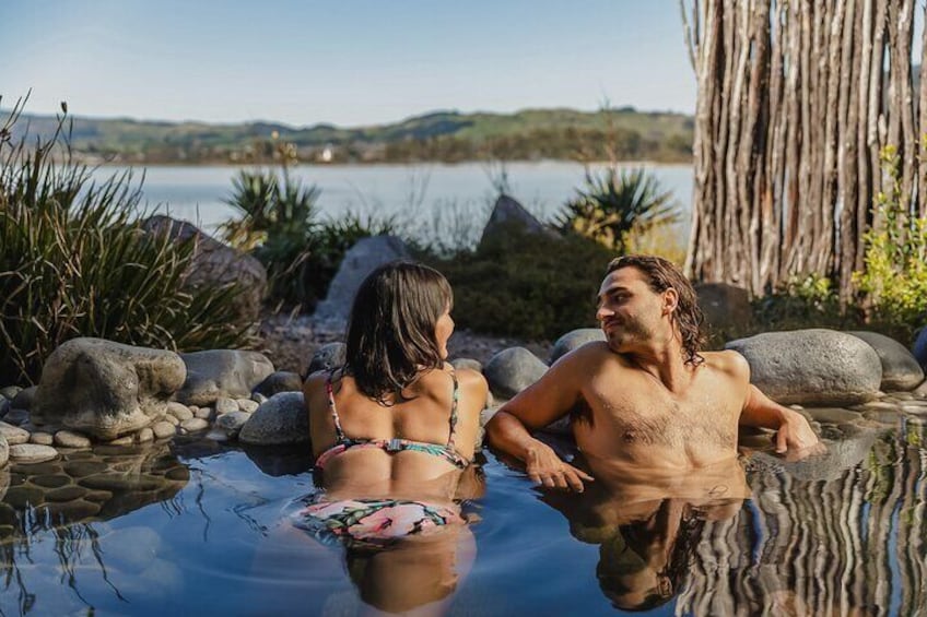 Two people in a hot spring surrounded by rocks and plants. 3