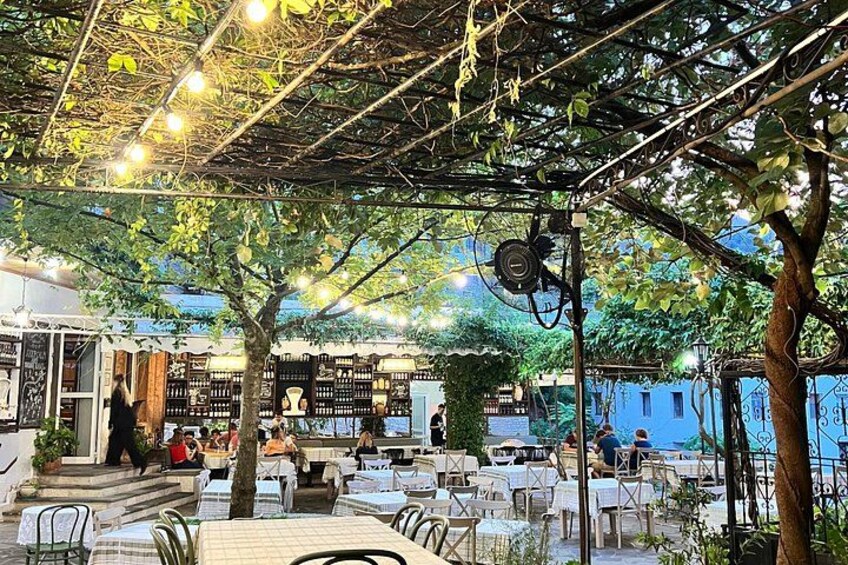 Een terras met tafels en stoelen, omringd door bomen en een pergola met lichtjes. 5