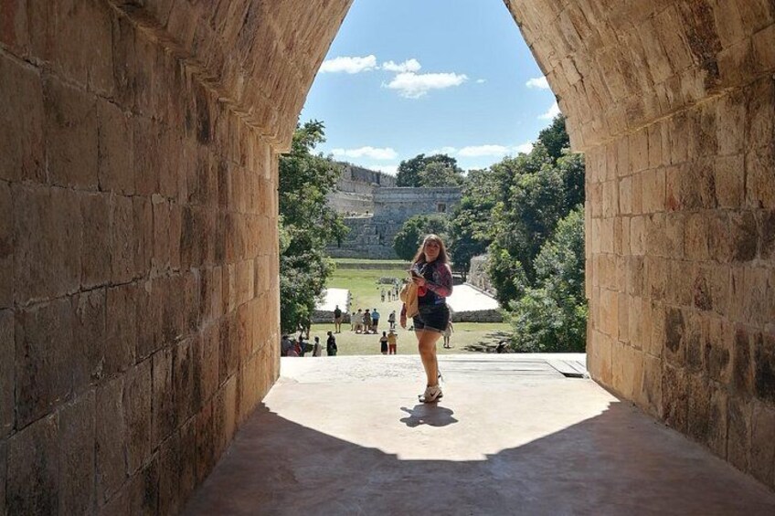 Un arco de piedra con una persona en su interior, mirando un sitio histórico con visitantes al fondo. 1