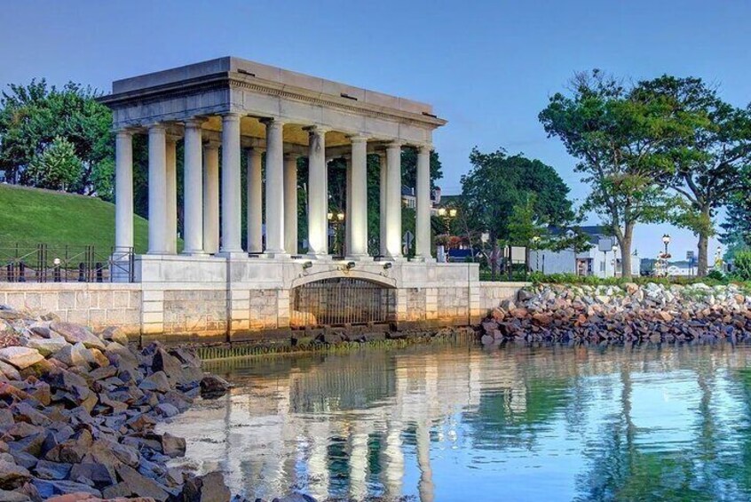 A neoclassical building with columns, a reflecting pool, and a stone wall. 4