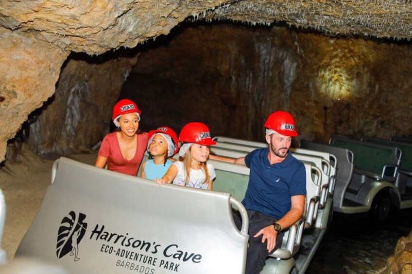 A cave tour with visitors wearing red helmets, a sign for Harrison's Cave, and a green vehicle. 1