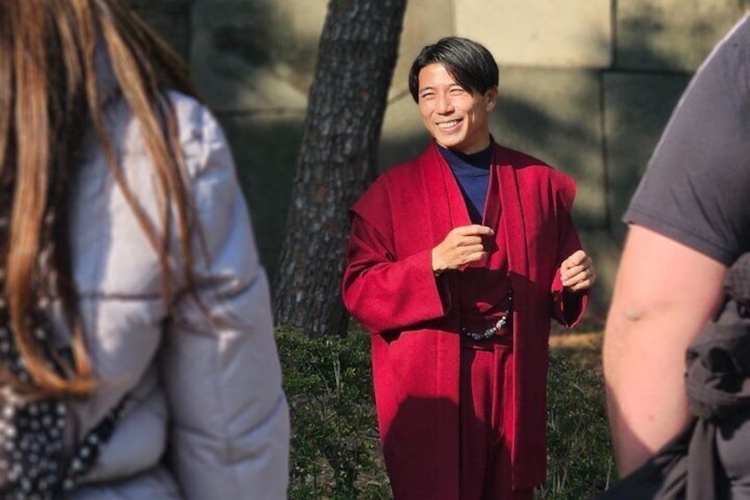A person in a red coat standing outdoors with trees and a building in the background. 5