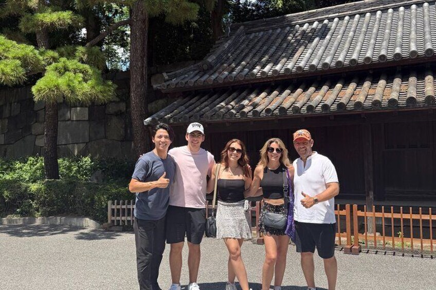 A group of people standing in front of a traditional Japanese building with a tiled roof and stone walls. 2