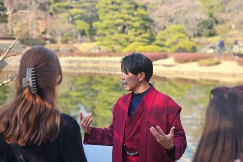 A person in a red coat gesturing, with a body of water and trees in the background. 3