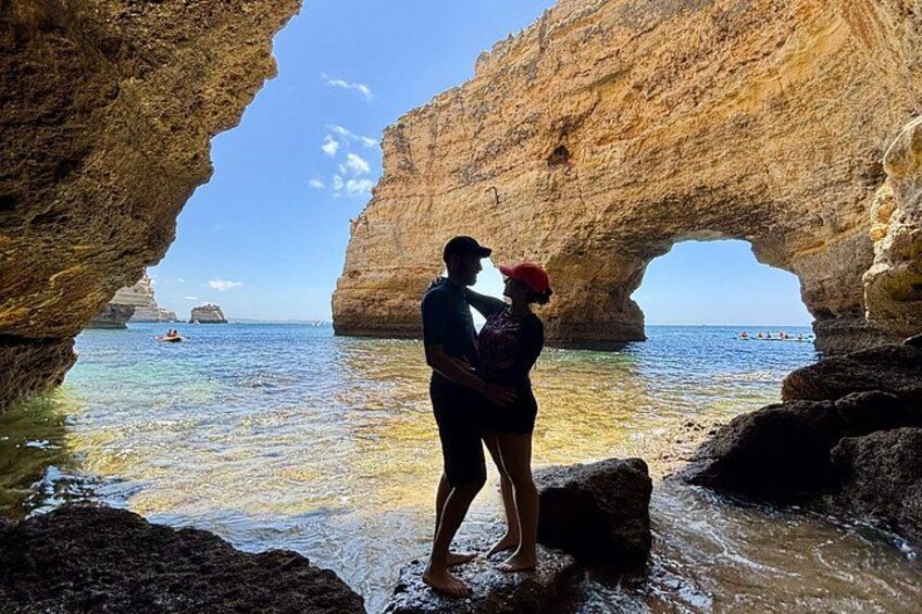 Una pareja de pie en una zona costera rocosa con una formación arqueada natural. 2