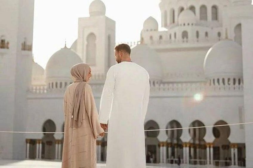 A couple holding hands in front of a white mosque with domes and minarets. 1
