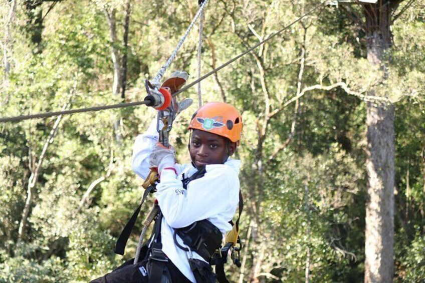 Una persona con chaqueta blanca y casco naranja haciendo tirolesa por un bosque. 5