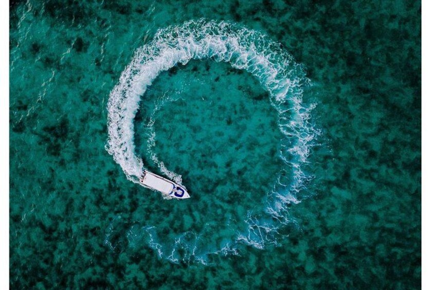 Una vista aerea di una barca che crea un disegno circolare nell'acqua turchese. 1