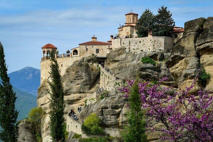 A monastery perched on a rocky cliff with a tower and a staircase leading up to it. 5