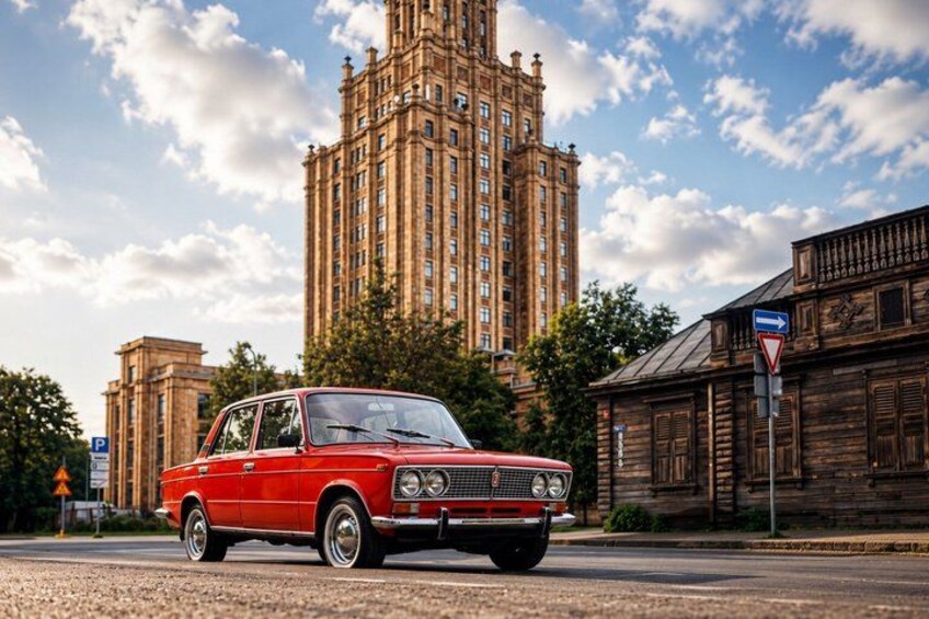 A red vintage car parked on a street with a tall building in the background. 1