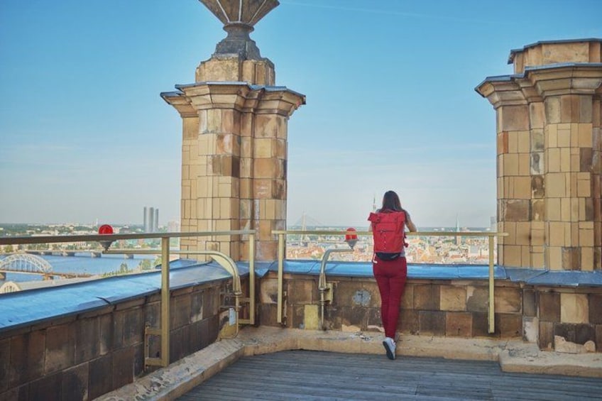 A person in red attire standing on a rooftop with a view of a cityscape, including a prominent tower structure. 2