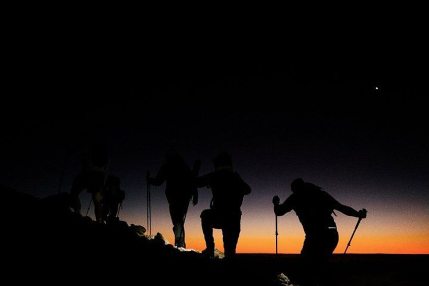 Un groupe de personnes faisant une randonnée au crépuscule, avec un coucher de soleil en arrière-plan. 2