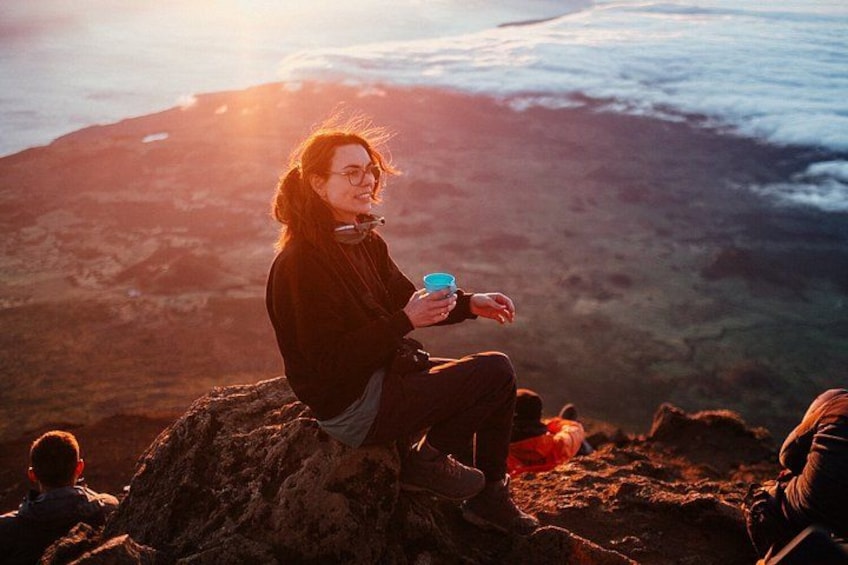 Une personne assise sur un rocher, une tasse à la main, et qui contemple un paysage montagneux. 1