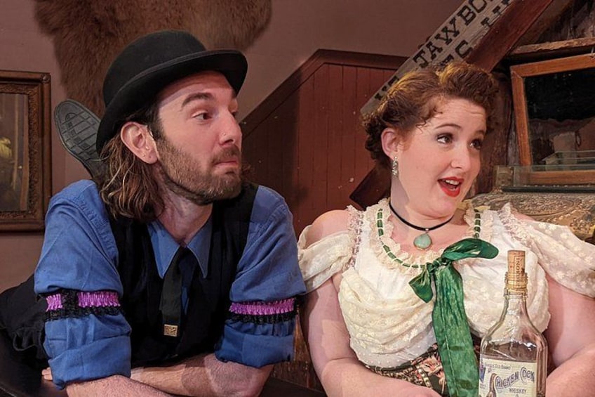 Two people in vintage costumes, one with a hat and vest, the other in a dress with a green scarf. 2