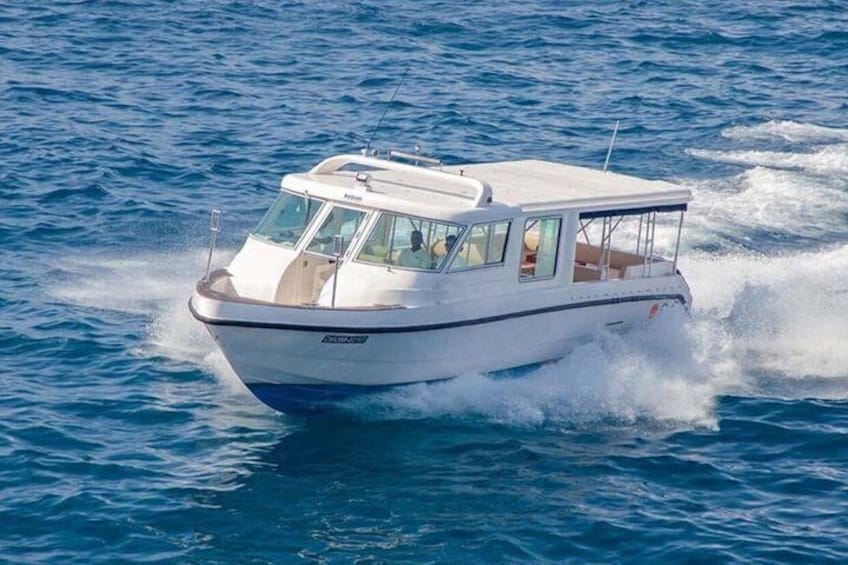 Ein weißes Motorboot mit Kabine und blauem Rumpf fährt durch blaues Wasser. 2