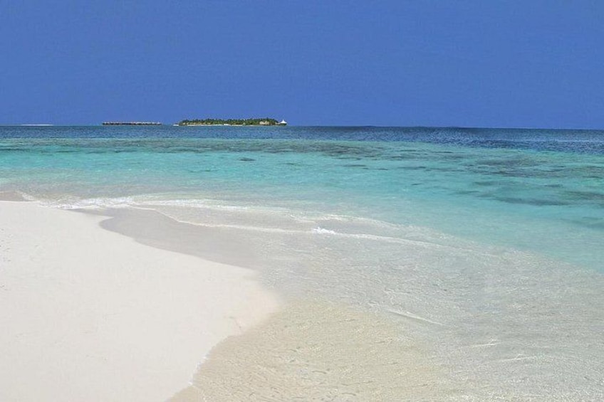 A beach with clear turquoise water, white sand, and a small island in the distance. 2