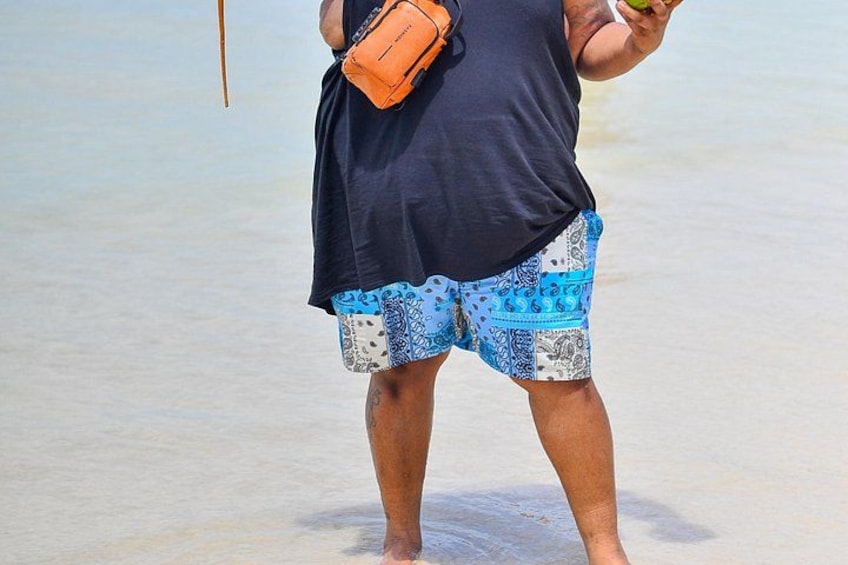 A person standing on a beach wearing a black top and patterned shorts, holding a green object. 5