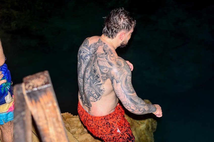 A person with tattoos standing on a rocky surface. 4