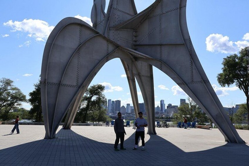 A large metallic sculpture in an open plaza with a city skyline in the background. 2