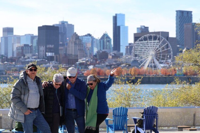 A group of people standing by a waterfront with a city skyline and a Ferris wheel in the background. 1