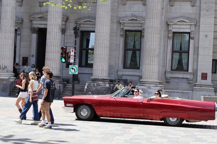 A red convertible driving past a classical building with columns. 4