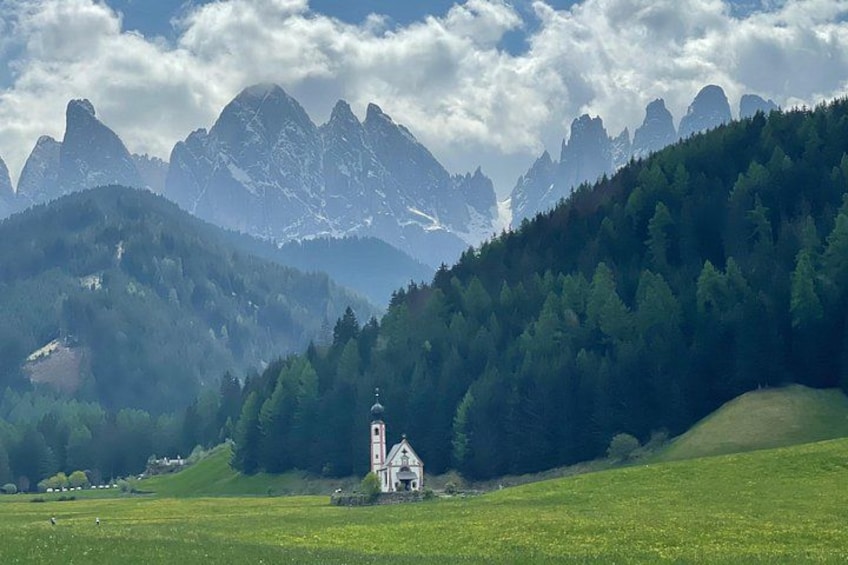 A church in a green field with mountains in the background. 2