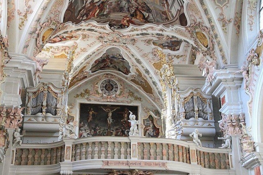 An ornate church interior with elaborate frescoes, a large organ, and a statue of Jesus Christ. 5